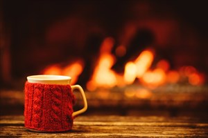 Mug in red knitted mitten standing near fireside.