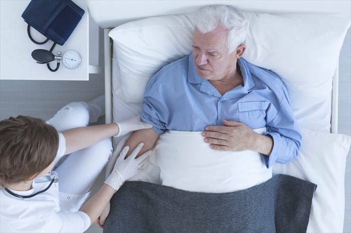 Nurse treating a senior patient lying on a hospital bed.