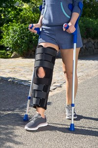 Woman walking and wearing a leg brace with adjustable side panels to immobilize and support her knee after surgery.