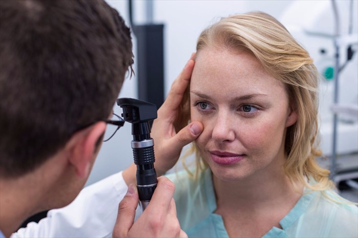 Optometrist examining a female patient through ophthalmoscope.