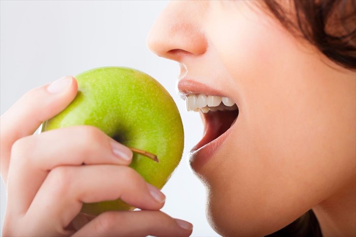 Young woman bites into a fresh apple (close-up).