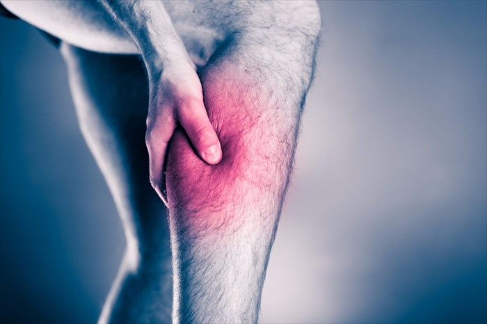 Male athlete holding leg with a painful red spot.