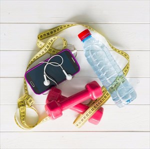 Fitness weights, measuring tape, phone and water bottle for exercise session.