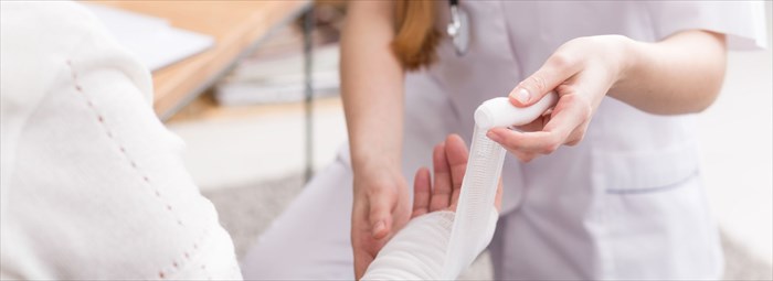 Close-up of young nurse dressing a woman's wound on the hand.