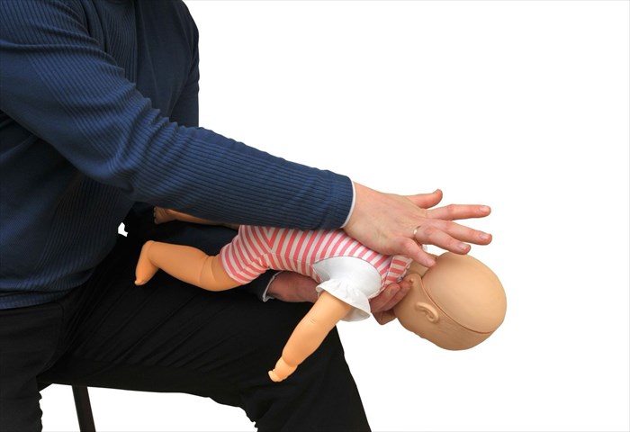 First aid instructor using infant dummy and demonstrating first aid for choking (back blows).