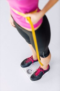 Young woman standing on the scale with measuring tape assessing her weight loss progress.