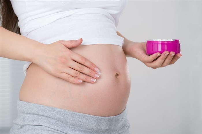 Close-up of pregnant woman applying stretch mark cream on her belly.