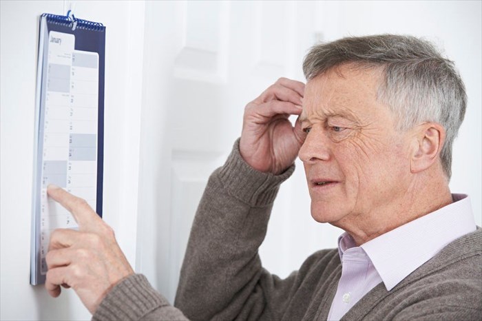 Confused senior man with dementia looking at wall calendar