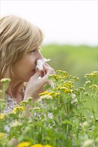 Woman blowing her nose into a tissue outdoors (allergy)