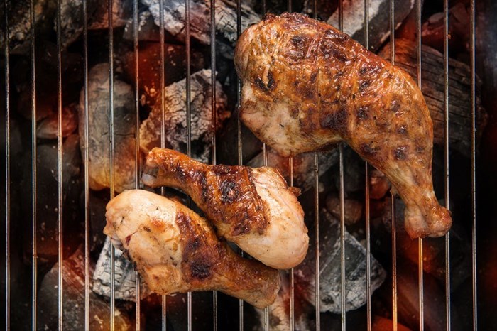 Grilled chicken thigh over flames on a barbecue.