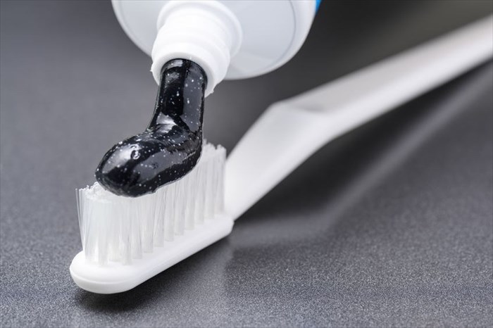 Close-up view of black charcoal whitening toothpaste being squeezed onto a white toothbrush.