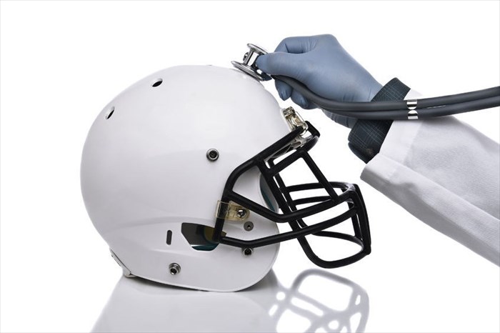 Close-up of a football helmet and a doctor's hand holding a stethoscope...