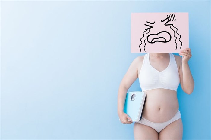 Overweight woman holding a 'crying board' over her face and a scale to illustrate unsuccessful weight loss efforts.