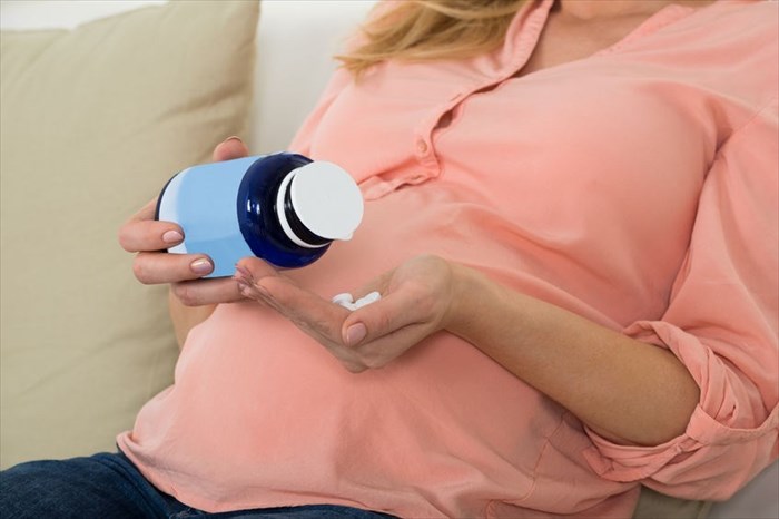 Midsection of a pregnant woman pouring pills into her hand.