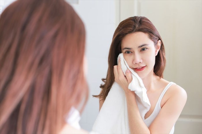 Young woman wiping her face with towel in bathroom.