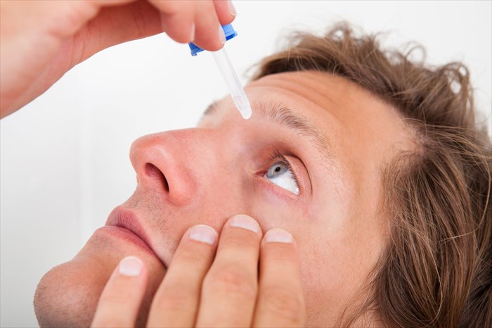 Close-up of a young man putting eye drops in his eyes.