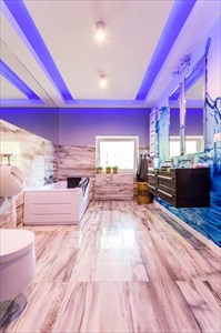 LED lighting in a spacious villa bathroom with marble tiling, toilet, bidet, bathtub, two basins and two mirrors.