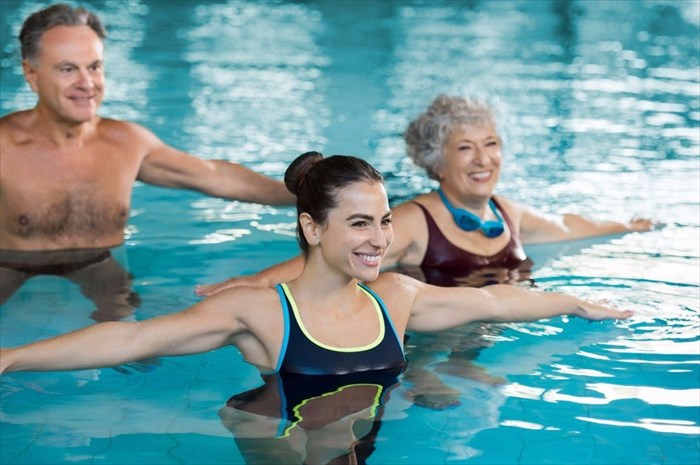 Smiling fitness class doing aqua aerobics in a swimming pool.